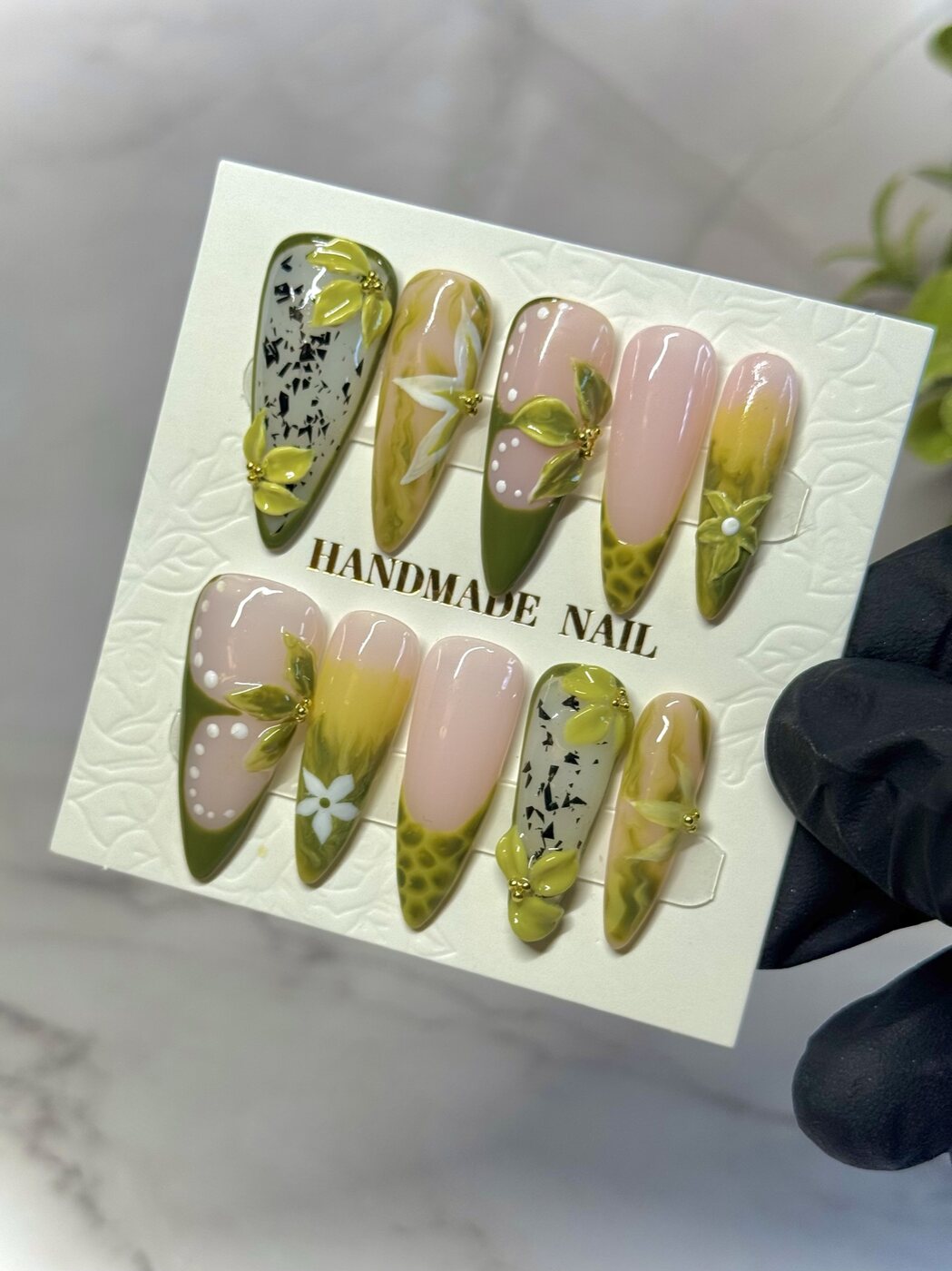 Pointed press-on nails with green floral art, soft pink bases and dimensional petals